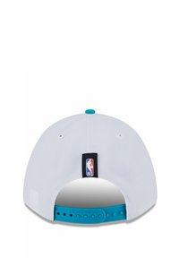 Weißer Baseballcap mit flachem Schirm, ausgestattet mit einem blauen Snap-Verschluss und einem kleinen NBA-Logo-Tag auf der Rückseite. Strukturiertes Material, glatte Oberfläche.