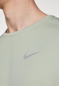 Světle zelené sportovní tričko s kulatým výstřihem, na hrudi s malým šedým logem Nike swoosh a texturovaným povrchem.