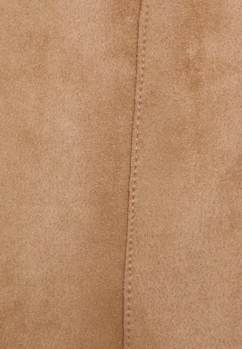 Tessuto scamosciato di un color beige chiaro, con una superficie liscia e dettagli di cucitura visibili lungo la cucitura.
