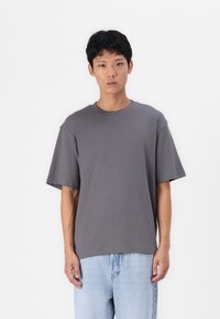 Tricou gri cu guler rotund, mâneci scurte, croială lejeră, fabricat dintr-un amestec de bumbac, asortat cu blugi din denim de culoare albastră deschisă.