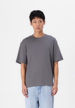 Gray crew neck t-shirt with short sleeves, relaxed fit, made of cotton blend fabric, paired with light blue denim jeans.