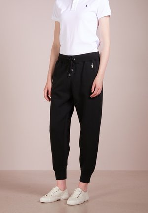 Pantaloni della tuta neri con vita regolabile, gambe affusolate e polsini a costine. Abbinati a una polo bianca e sneaker color crema.