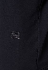 Černá bavlněná košile s texturovanou látkou, na boku s obdélníkovou černou koženou nášivkou s vystouplým textem.