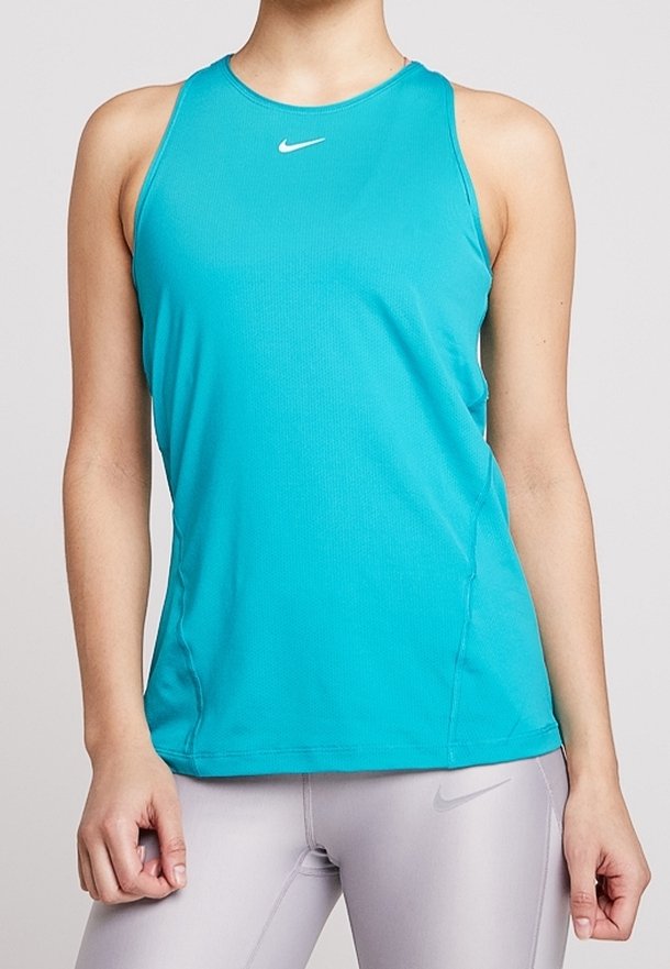 Žena v tílku v tyrkysové barvě a světle šedých legínách, obě s logem Nike, stojí s uvolněnýma rukama.