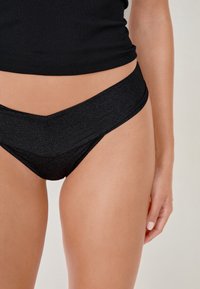 Slip da bikini neri con un design a vita alta, texture liscia e una finitura leggermente scintillante. Presentano una vita a forma di V.