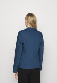 Blazer entallado en azul marino con un diseño estructurado, abertura trasera sencilla y detalle de seis botones en los puños, confeccionado en tejido suave.