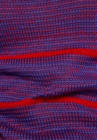Strickstoff in Lila mit roten Akzenten. Verfügt über eine strukturierte Oberfläche und abwechselnde Streifen, die eine Mischung aus Fasern und Farben zeigen.
