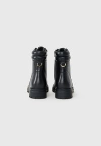 Botas de tobillo de cuero negro con punta redondeada, cuello suavemente fruncido, detalles en metal dorado y suela de goma texturizada.