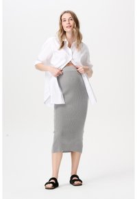 Witte blouse met knopen, kort gesneden bij de taille, gecombineerd met een geribbelde, grijze rok tot op de knie. Zwarte sandalen met twee banden.