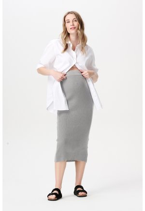 Witte blouse met knopen, kort gesneden bij de taille, gecombineerd met een geribbelde, grijze rok tot op de knie. Zwarte sandalen met twee banden.