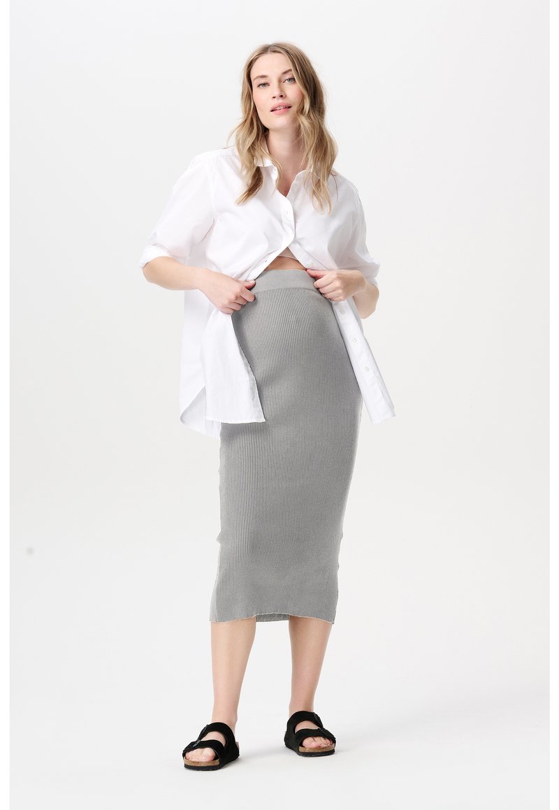 Witte blouse met knopen, kort gesneden bij de taille, gecombineerd met een geribbelde, grijze rok tot op de knie. Zwarte sandalen met twee banden.