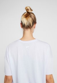 Camiseta blanca de manga corta con un corte relajado y escote redondo. Presenta un pequeño logo de Nike en blanco en la parte superior de la espalda. Textura suave.