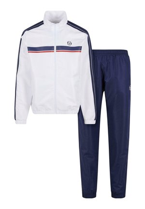 Veste blanche zippée avec des rayures bleu marine et rouge, associée à un pantalon de survêtement bleu marine avec une taille élastique et des chevilles resserrées.