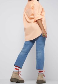 Camicia rosa pallido a taglio largo, jeans in denim blu chiaro, stivaletti beige con suola spessa, lacci rossi e calzini a righe. Outfit semplice e informale.