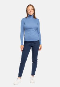 Maglia a collo alto a maniche lunghe di colore azzurro abbinata a jeans skinny blu scuro e sneaker bianche. Tessuto morbido con un design aderente.