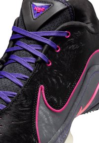 Zapato deportivo negro con parte superior texturizada, cordones morados, detalles en rosa y un panel gris liso. Logo de diamante destacado en la lengüeta.