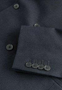 Tume meriino bleiseri, millel on tekstuuriga viimistlus. Varrukatel on viis musta nuppu, mis täiustavad stiilset ja kohandatud disaini.