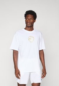 Hvit kortermet t-skjorte i bomull med en gull Nike-logo innenfor et sirkulært design. Skjorten har en avslappet passform og myk tekstur.