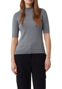 Szary sweter z krótkim rękawem, wykonany z dzianiny, z wysokim dekoltem oraz żebrowanymi mankietami i dolnym wykończeniem. Gładka tekstura; dopasowany krój. Połączony z ciemnymi spodniami cargo.