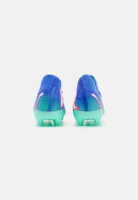 Botas de fútbol con parte superior de malla texturizada azul, acentos en rosa y verde, y suela de goma transparente. Presenta un diseño ligero y flexible.