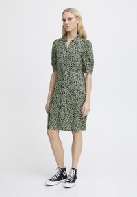 Abito a fiori verde e nero, maniche corte, con bottoni sul davanti, lunghezza al ginocchio, abbinato a sneakers alte nere.