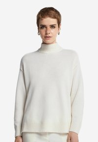 Cremefarbener Rollkragenpullover aus weichem, strukturiertem Material; verfügt über einen gerippten Kragen und Saum, hat eine lockere Passform und überschnittene Schultern.