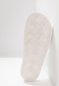 Valkoinen kumin kengänpohja, jossa on kuusikulmainen kuvio, kohotettu tekstuuri ja kohokuvioitu "EA"-logo, vinossa kevyttä taustaa vasten.