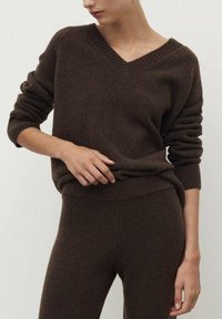 Brauner Wollpullover mit V-Ausschnitt, gerippten Bündchen und Saum, kombiniert mit passenden braunen, taillierten Hosen, die eine weiche Textur und einen lockeren Schnitt aufweisen.