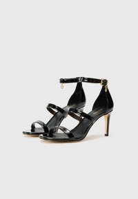 Crne lakirane cipele s potpeticom s tri horizontalne trake, trakom oko gležnja i zlatnim ukrasnim detaljem. Potpetica stiletto ima elegantan dizajn.