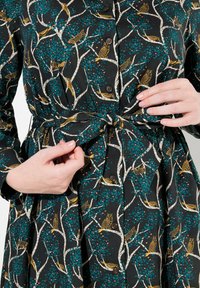 Abito nero con un motivo di uccelli e rami d'albero in teal e oro. Presenta una chiusura con bottoni e una cintura in tessuto in vita.