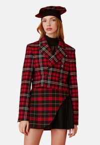 Rood en zwart geruite dubbelgebreide blazer met brede revers, gecombineerd met een bijpassende rok met plooien en een asymmetrische zoom.