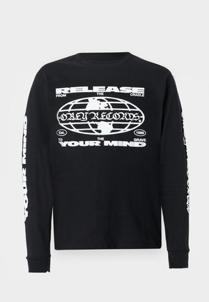 Juoda ilgomis rankovėmis marškinėliai su balta gaublio grafika ir užrašu „Išlaisvink mintis nuo lopšio iki kapo“ bei „Obey Records įkurta 1989 m.“