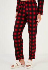 Pantalones de pijama en cuadros rojos y negros con una cintura elástica. Tejido suave, diseño de pierna recta. Llevados con zapatillas de casa blancas y acogedoras.