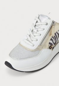 Sneaker bianca con accenti metallici argento e oro, pannelli testurizzati, una zip laterale e dettagli con stampa leopardata e zebra.