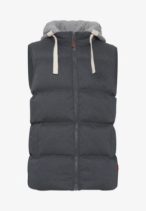 Harmaa paksu liivi, jossa on vetoketju edessä, harmaa huppu ja beige narut. Sisältää suuret tikatut alueet ja sivutaskun. Ruskea logo korostus.