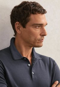 Naktiņkrekls jūras zilā krāsā ar īsām piedurknēm, fakturētu audumu, trīs pogu aizdares vietu un klasisku apkakli. Modelis attēlots profilā.