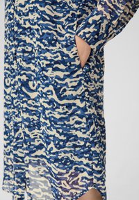 Robe longue à motifs abstraits bleus et crème, confectionnée en tissu léger, avec une poche et des détails de boutons.