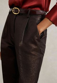 Mustat, teksturoidut housut, joissa on hieno kiilto ja sivutaskut. Yhdistetty punaisen paidan ja kiiltävän, tumman vyön kanssa, jossa on kultainen solki.