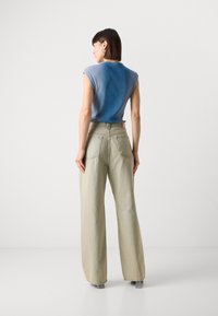 Haut côtelé bleu clair à manches courtes associé à un pantalon taille haute, large, vert pâle. Poches arrière visibles sur le pantalon.