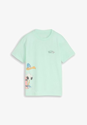 Chemise vert clair à manches courtes avec le texte "LET'S RIDE" et un oiseau souriant portant un bonnet bleu et des baskets tenant un skateboard rose.