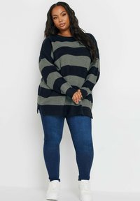 Stickad tröja med gröna och marinblå horisontella ränder, ribbad struktur och sidofickor. Tillsammans med blå jeans och vita sneakers.