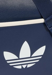 Granatowa skórzana torba z dużym białym logo Trefoil oraz trzema poziomymi paskami. Torba ma teksturowaną powierzchnię i kremowe akcenty.