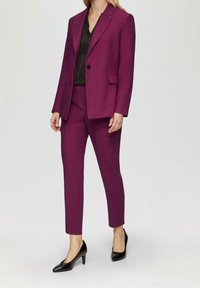 Magenta kostym med en skräddarsydd blazer och smala byxor, i kombination med en svart blus och svarta högklackade skor. Slätt tyg med klassisk design.