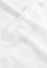Witte katoenen t-shirt met ronde hals en subtiele geborduurde logo in lichtgrijze tekst, met een gladde, effen textuur.
