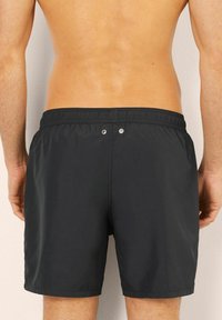 Svarta simshorts med lös passform, elastisk midja och två öljettdetaljer bak. Tillverkade av lätt, slätt tyg.