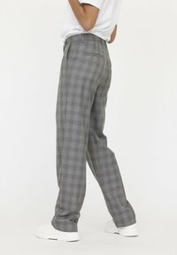 Grijze geruite broeken met een recht gesneden ontwerp, voorzakken en een gladde stoftextuur. Gecombineerd met witte sneakers.