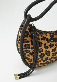 Torba životinjskog uzorka s leopard printom u nijansama smeđe i crne. Glatki crni kožni remeni i zatvaranje na munju na vrhu.