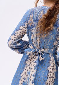 Vloeiende blauwe jurk met paisleypatronen, lange mouwen en een strik in de taille. Soepele stof met een gedetailleerd, contrasterend ontwerp.