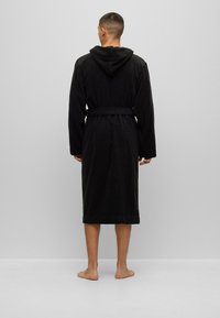 Black cotton bathrobe with a hood, long sleeves, and a tie waist, reaching mid-calf. Soft texture, simple design, no visible patterns.