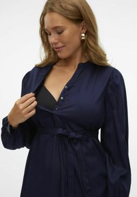 Vestido azul marino con escote abotonado, mangas largas abullonadas y cintura atada. El material parece suave con un brillo sutil.